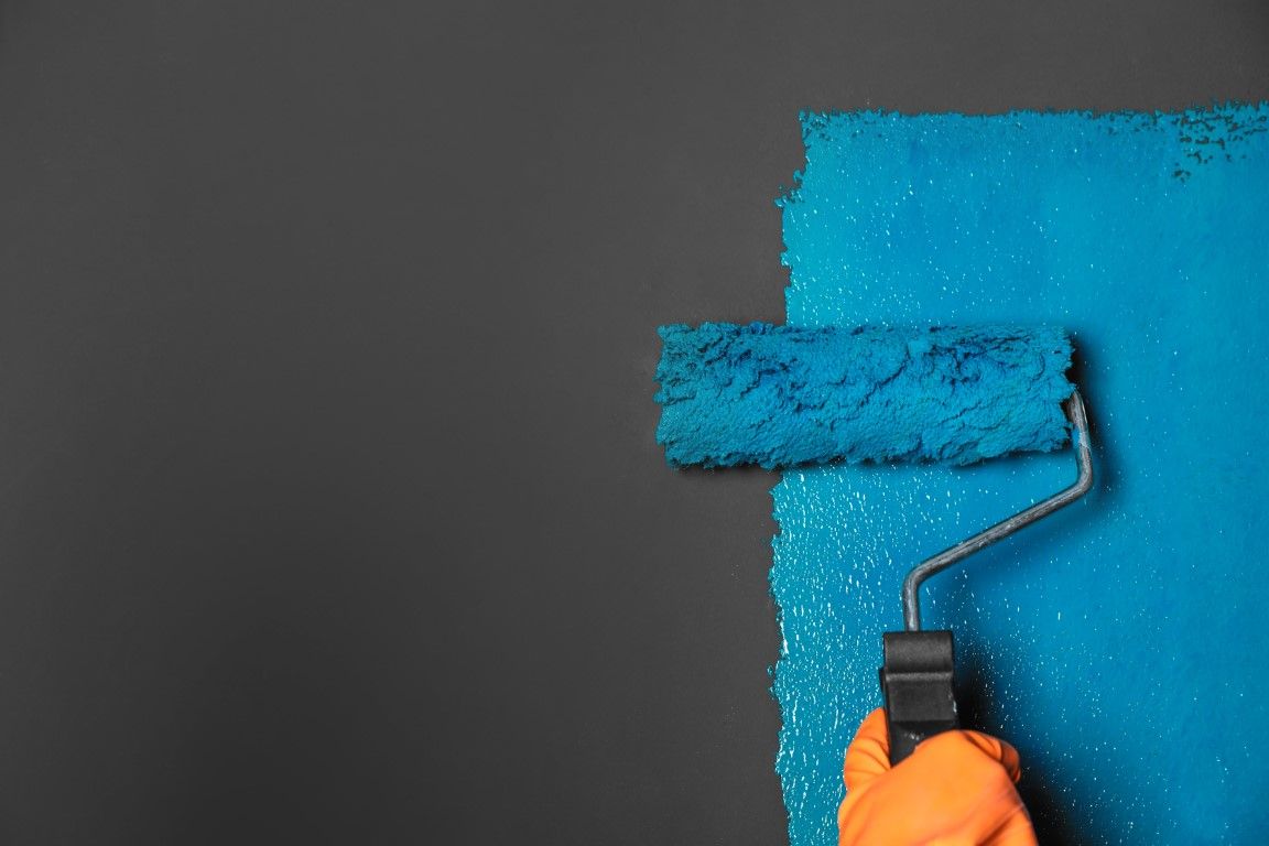 Close-up of a wide roller on a dark wall, gloved hand